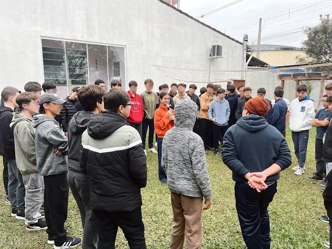 Júlia conduzindo uma dinâmica em roda com um grupo de adolescentes no pátio da escola